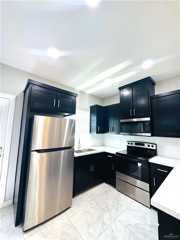 Kitchen with stainless steel appliances, light marble finish floors, light countertops, and dark cabinets