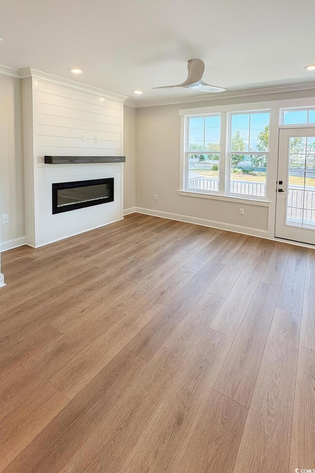 Unfurnished living room featuring recessed lighting, ornamental molding, light wood-style flooring, a glass covered fireplace, and ceiling fan