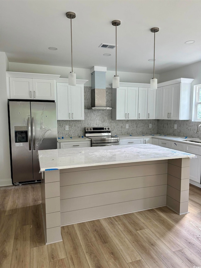 Kitchen with appliances with stainless steel finishes, wall chimney exhaust hood, white cabinets, decorative backsplash, and light wood-style flooring