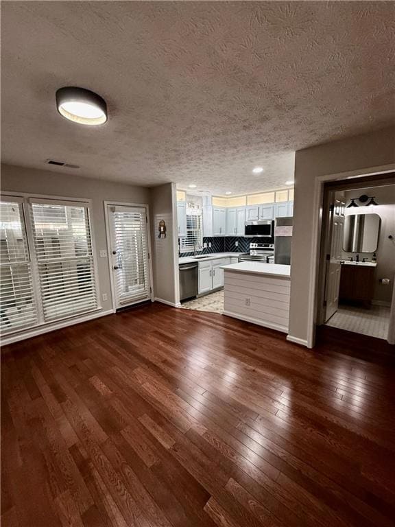 Kitchen featuring white cabinetry, light countertops, dark wood-style floors, a textured ceiling, and open floor plan