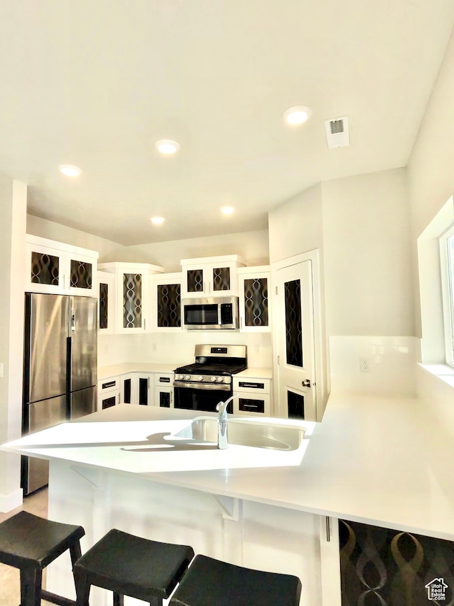 Kitchen featuring a kitchen bar, a peninsula, white cabinetry, stainless steel appliances, and recessed lighting