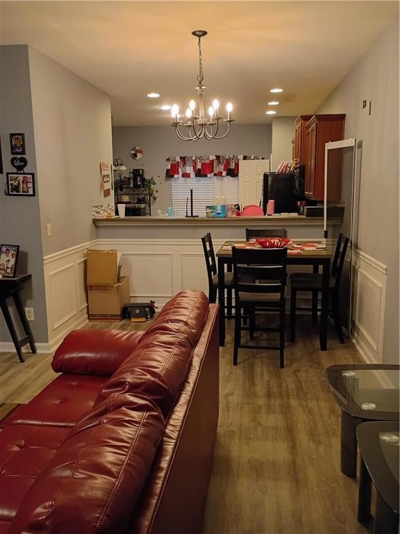 Living room featuring a decorative wall, wainscoting, wood finished floors, a chandelier, and recessed lighting