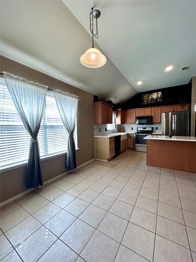 Kitchen featuring light countertops, lofted ceiling, pendant lighting, light tile patterned flooring, and black appliances
