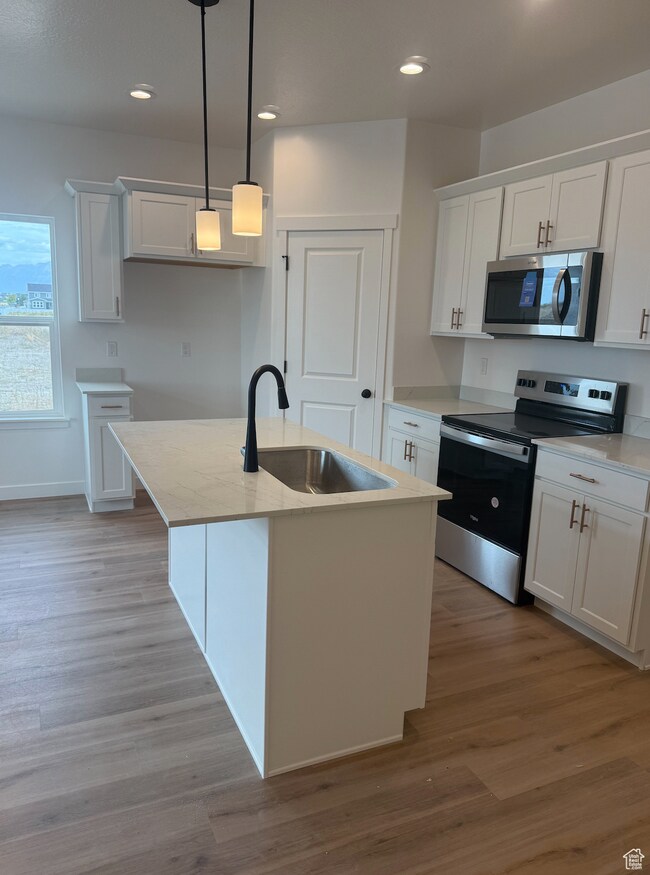 Kitchen featuring stainless steel appliances, white cabinets, pendant lighting, a kitchen island with sink, and light wood-type flooring