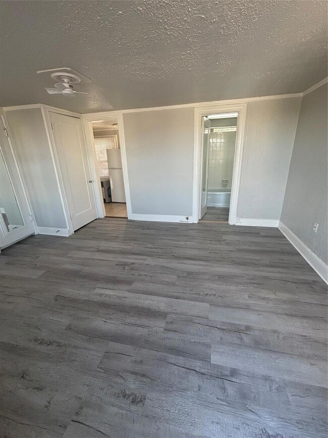 Unfurnished bedroom featuring hardwood / wood-style flooring, connected bathroom, refrigerator, and a textured ceiling