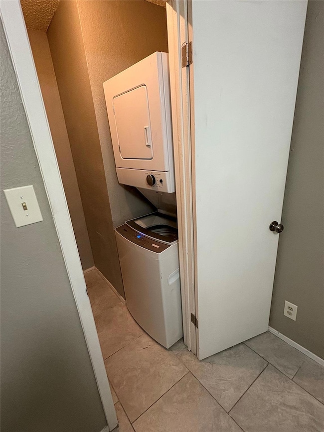 Washroom with stacked washer and clothes dryer, light tile patterned floors, and a textured wall