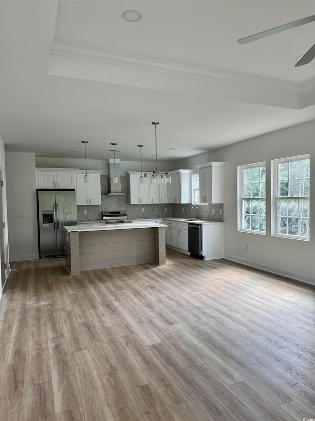 Kitchen featuring stainless steel appliances, ornamental molding, a center island, light wood finished floors, and light countertops