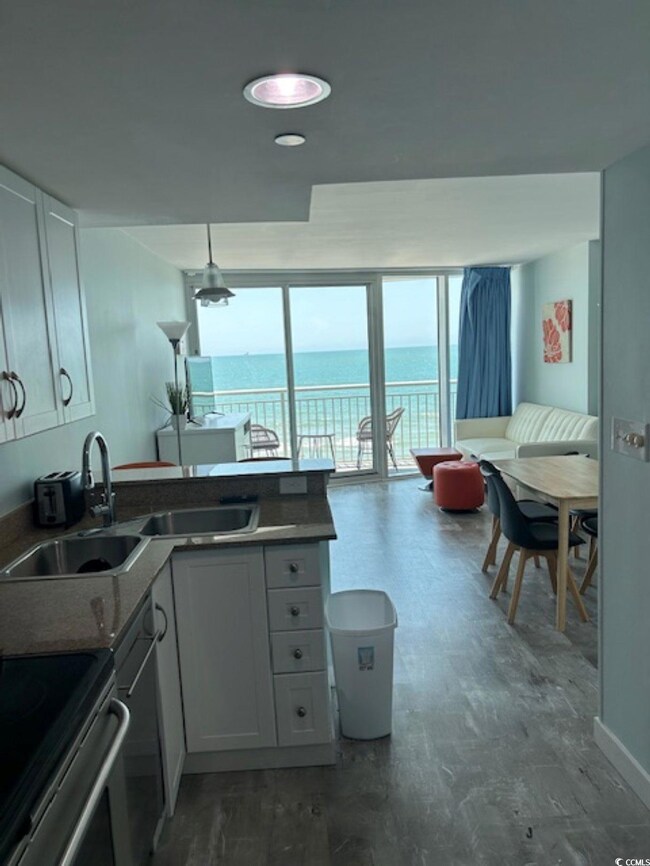 Kitchen with white cabinets, wood finished floors, a wall of windows, a peninsula, and dark countertops