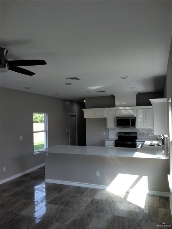 Kitchen with a sink, a ceiling fan, stove, baseboards, and white cabinets