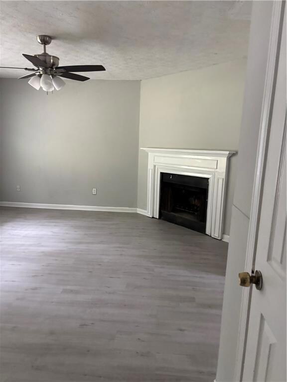 Unfurnished living room with a ceiling fan, wood finished floors, a textured ceiling, a fireplace, and baseboards
