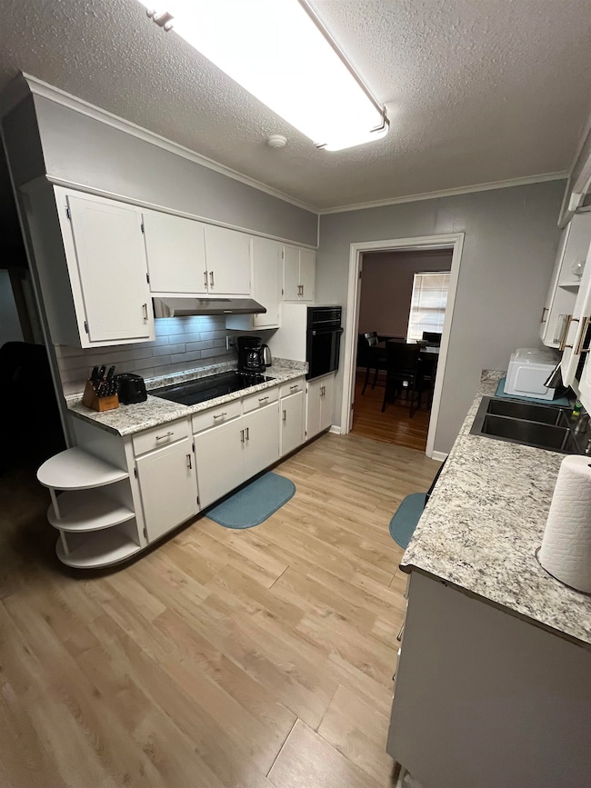 Kitchen with backsplash, light wood-style flooring, crown molding, white cabinetry, and a textured ceiling