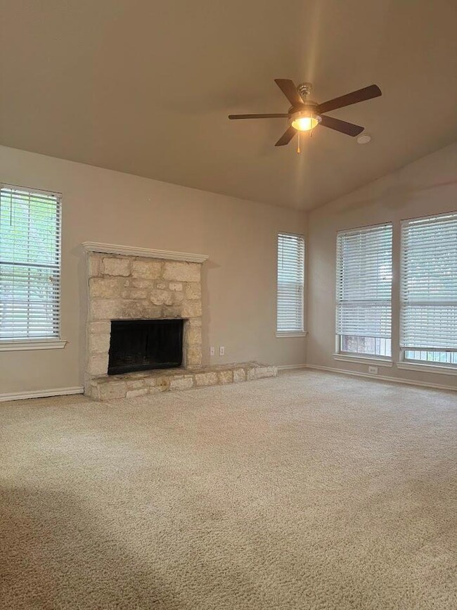 Unfurnished living room featuring a ceiling fan, carpet floors, vaulted ceiling, and a stone fireplace