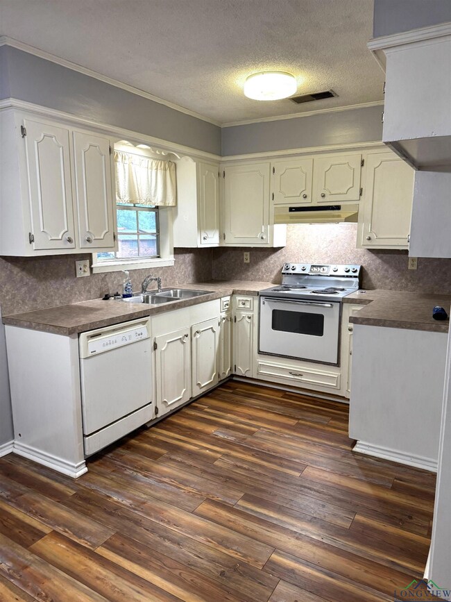 Kitchen featuring white appliances, under cabinet range hood, ornamental molding, dark countertops, and backsplash