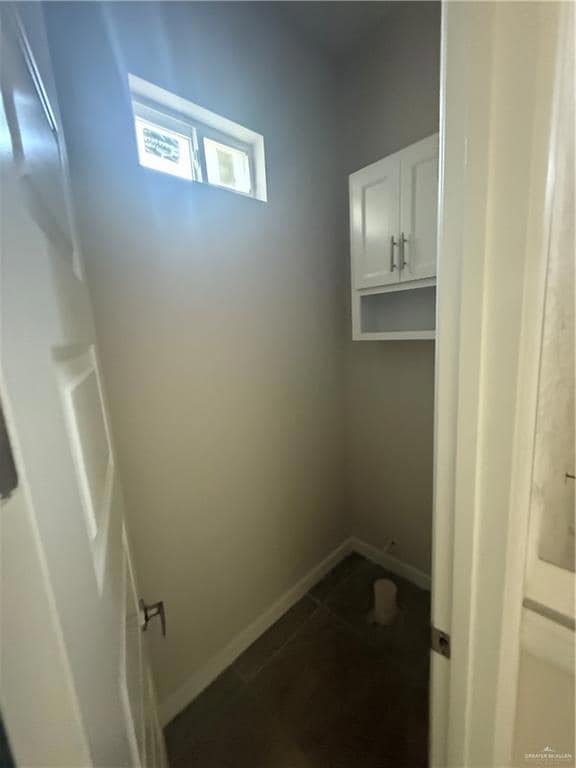 Laundry area with baseboards and dark tile patterned flooring