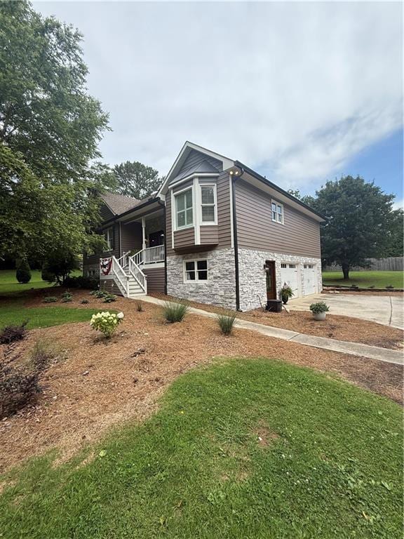 View of property exterior with stone siding, an attached garage, driveway, covered porch, and stairs