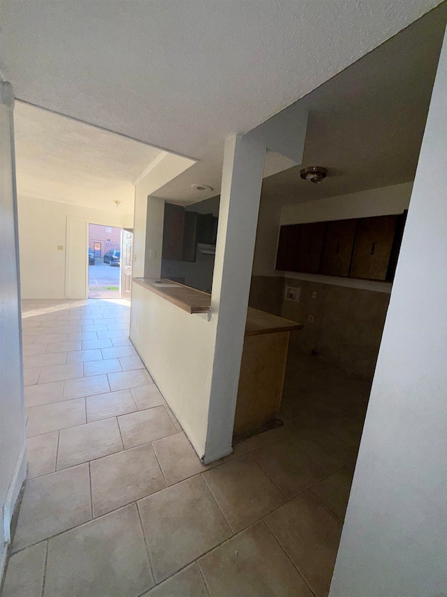 Hall with light tile patterned flooring and a textured ceiling