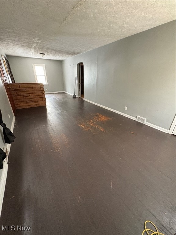 Unfurnished living room with arched walkways, dark wood-style flooring, and a textured ceiling