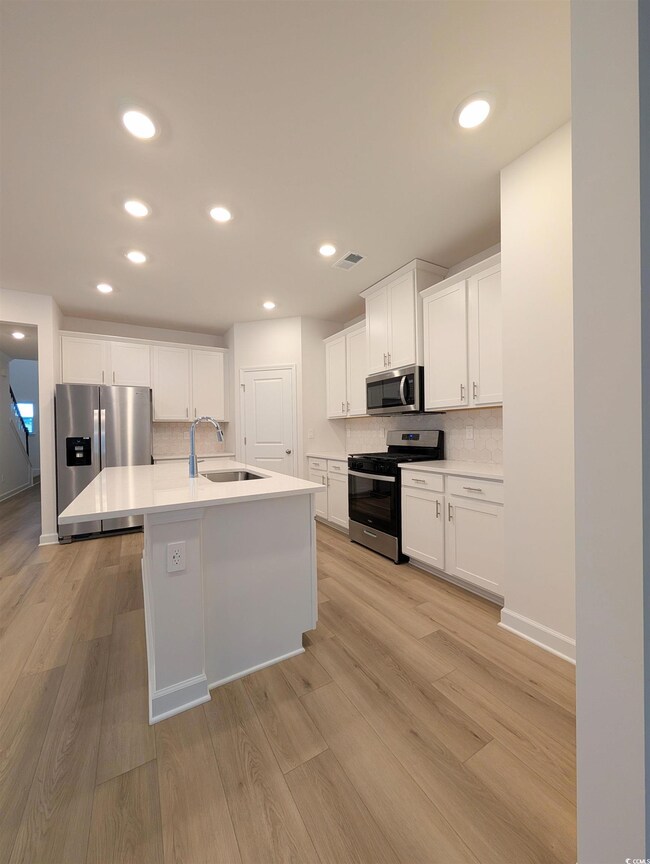 Kitchen with stainless steel appliances, white cabinetry, recessed lighting, backsplash, and a center island with sink