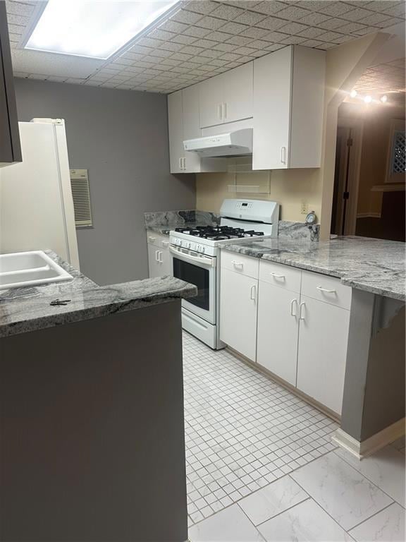 Kitchen with gas range gas stove, white cabinetry, fridge, and range hood