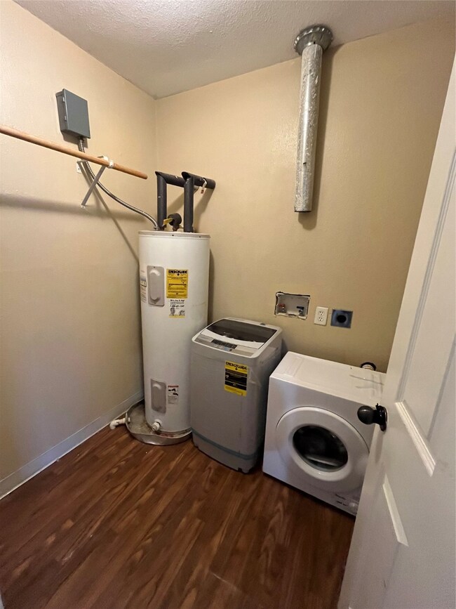 Washroom with dark wood-style floors, washer / dryer, water heater, and a textured ceiling