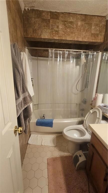 Bathroom with vanity, shower / bath combination with curtain, tile patterned flooring, toilet, and a textured ceiling