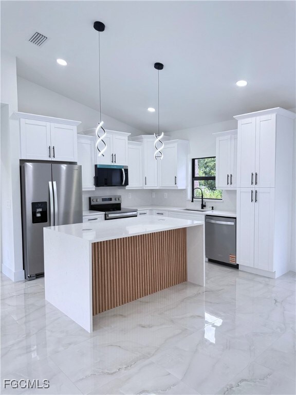 Kitchen with a center island, light marble finish floors, appliances with stainless steel finishes, hanging light fixtures, and lofted ceiling