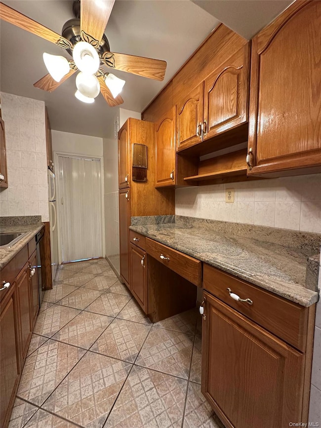 Kitchen with tasteful backsplash, brown cabinets, dark stone countertops, and a ceiling fan