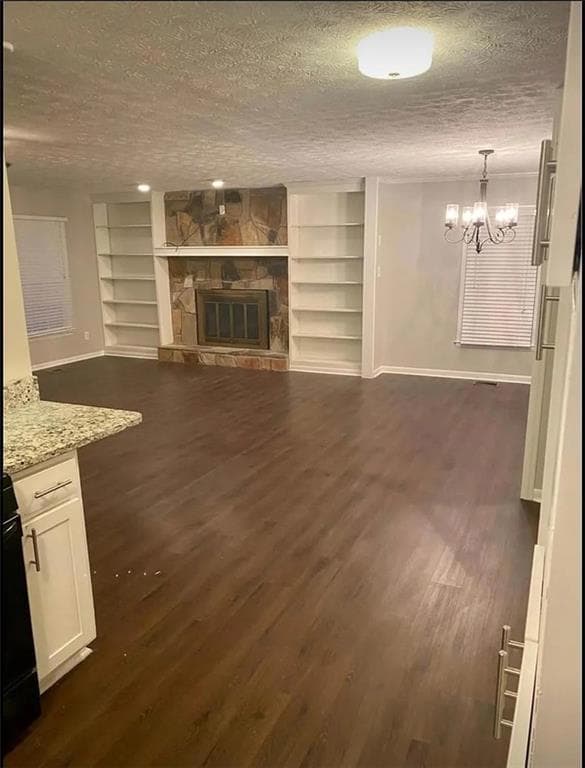 Unfurnished living room with baseboards, built in features, dark wood finished floors, and a textured ceiling
