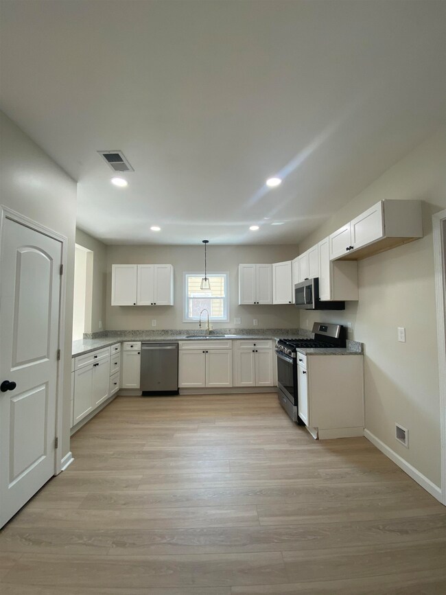 Kitchen with white cabinets, stainless steel appliances, recessed lighting, light wood-type flooring, and hanging light fixtures