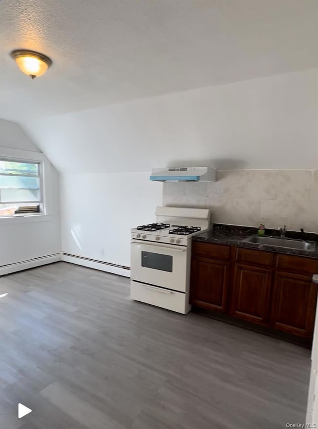 Kitchen with white range with gas cooktop, dark wood-type flooring, lofted ceiling, extractor fan, and baseboard heating