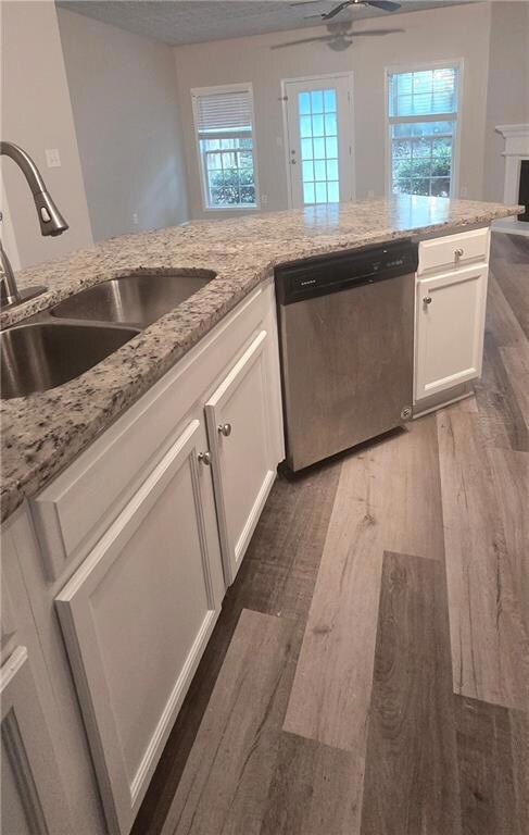 Kitchen featuring white cabinets, dark wood-style flooring, dishwasher, light stone counters, and a ceiling fan