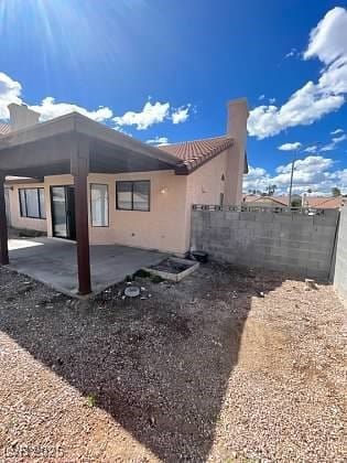 Rear view of house with a chimney, a patio, stucco