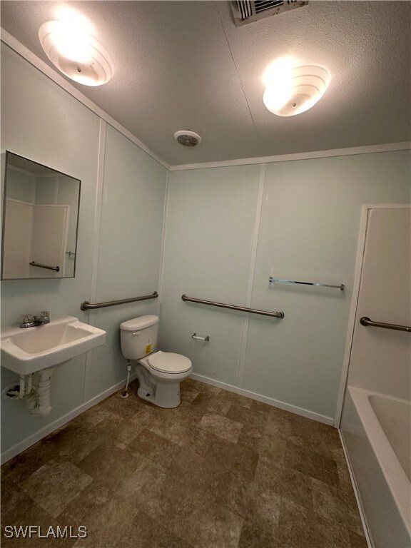 Bathroom featuring a textured ceiling, toilet, and sink
