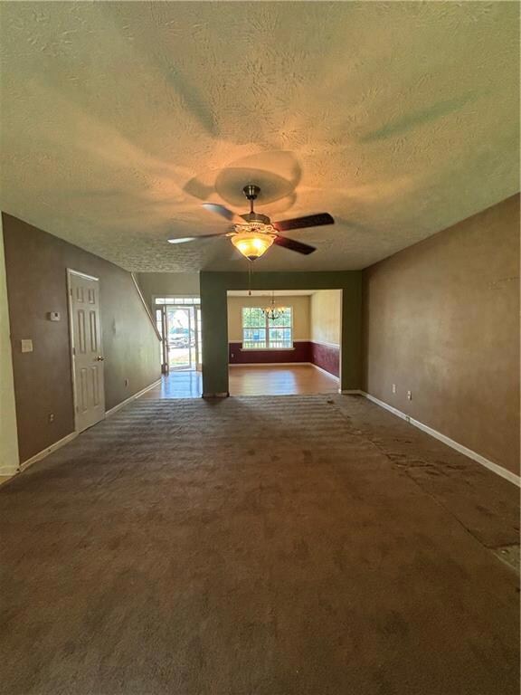 Unfurnished living room with a textured ceiling, dark colored carpet, a chandelier, and a ceiling fan