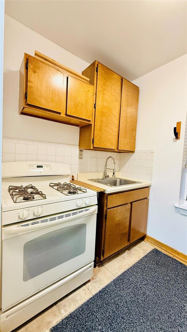 Kitchen featuring white gas range oven, brown cabinetry, decorative backsplash, light countertops, and light tile patterned floors