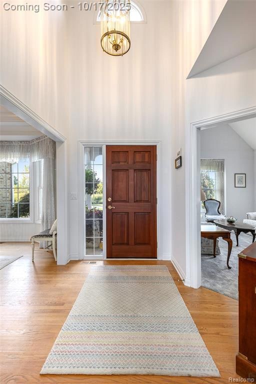 Foyer with light wood finished floors, a chandelier, and a towering ceiling