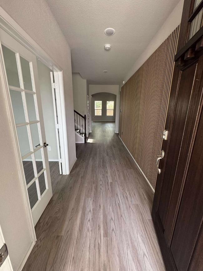 Hallway with wood finished floors, a textured ceiling, french doors, arched walkways, and stairs