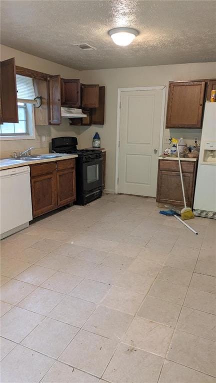 Kitchen with white appliances, a textured ceiling, light countertops, under cabinet range hood, and light tile patterned floors