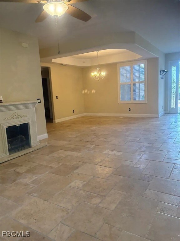 Unfurnished living room featuring a tray ceiling, ceiling fan, a glass covered fireplace, and a chandelier
