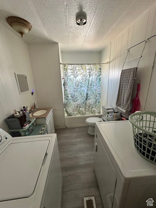Full bathroom featuring vanity, washer / dryer, shower / bath combo with shower curtain, dark wood finished floors, and a textured ceiling