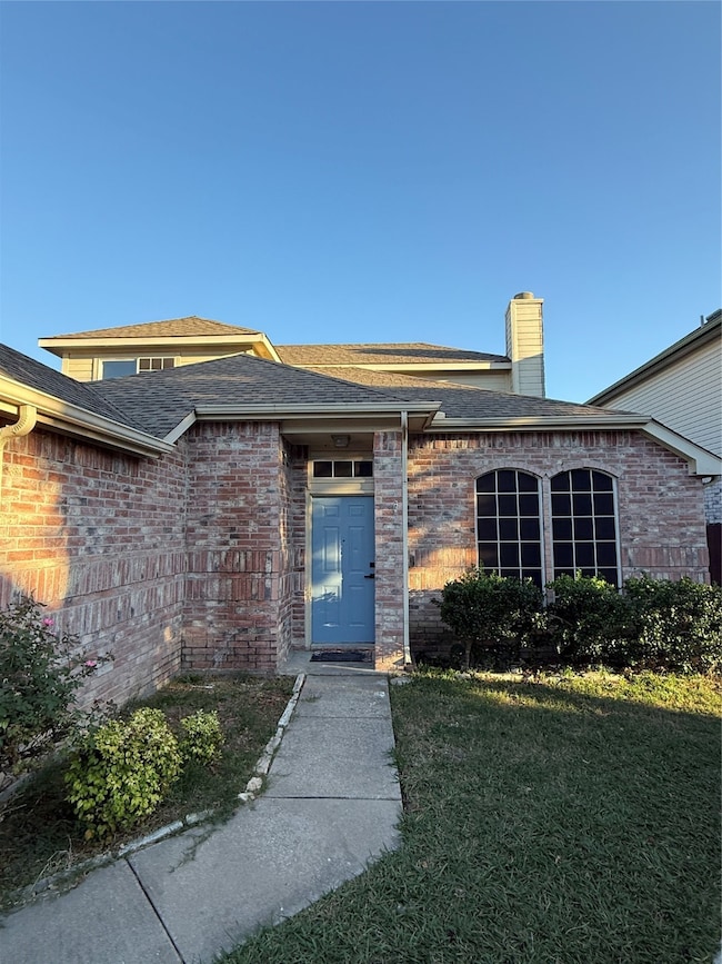 Doorway to property with roof with shingles, a lawn, brick siding, and a chimney