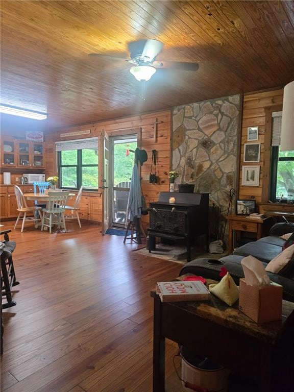 Living area featuring a wood stove, wooden walls, wood ceiling, ceiling fan, and wood-type flooring