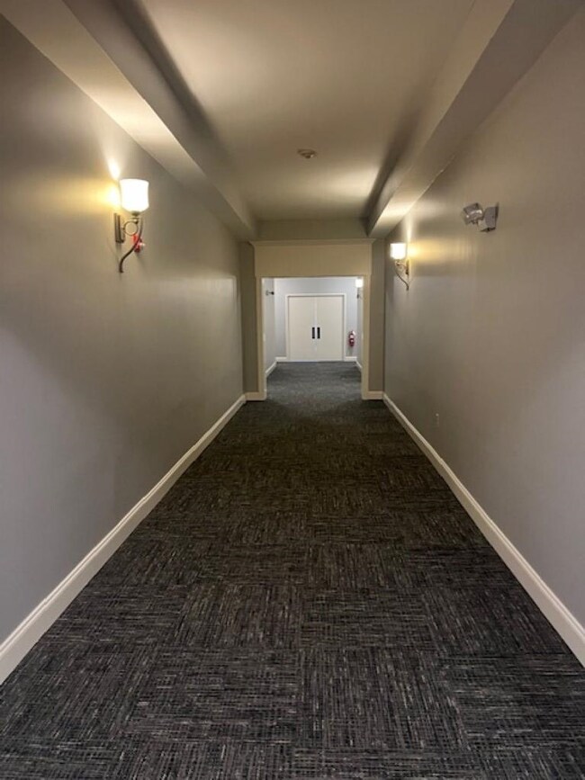 Hall featuring dark colored carpet