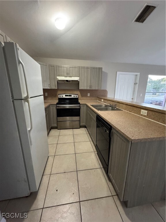 Kitchen featuring fridge, stainless steel electric range oven, light tile patterned floors, and extractor fan