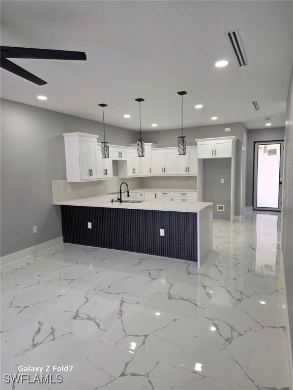 Kitchen with white cabinetry, a peninsula, recessed lighting, light marble finish floors, and hanging light fixtures