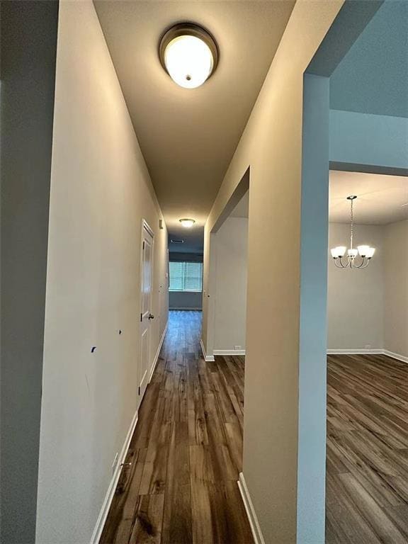 Hallway with dark wood finished floors and a chandelier