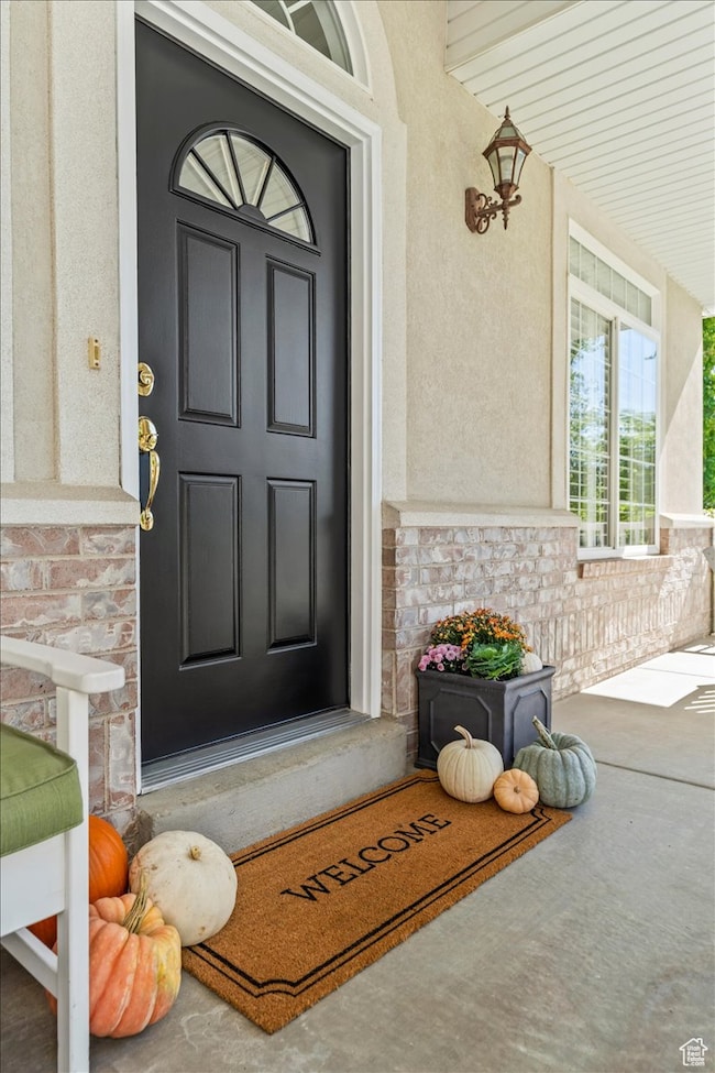 Doorway to property with stone siding, stucco siding, and covered porch