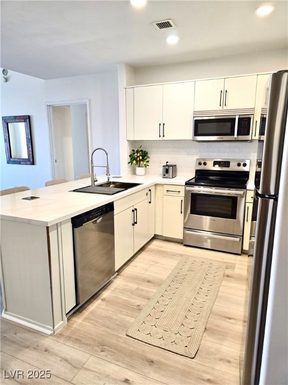 Kitchen with light countertops, stainless steel appliances, a kitchen breakfast bar, backsplash, and light wood finished floors