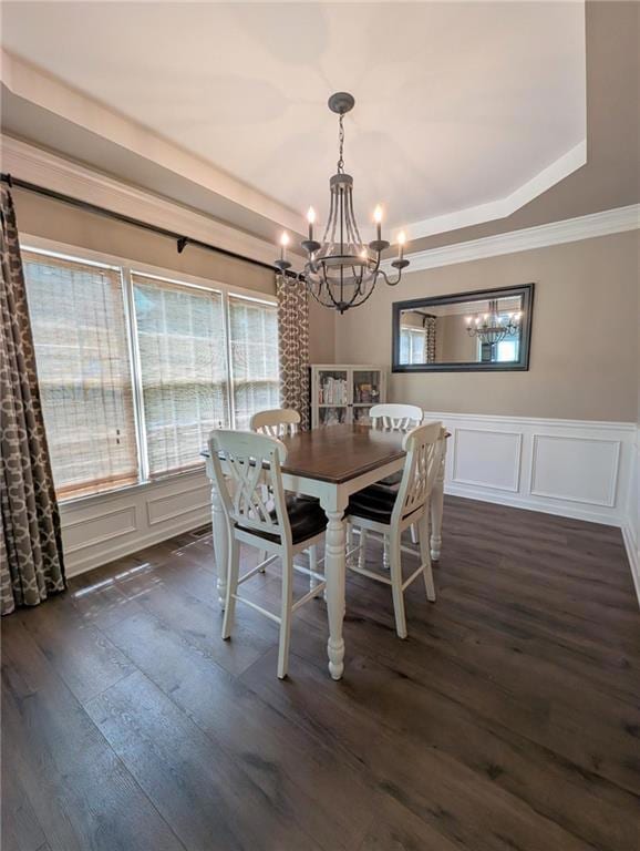 Dining room featuring a chandelier, a decorative wall, wainscoting, dark wood-type flooring, and a tray ceiling
