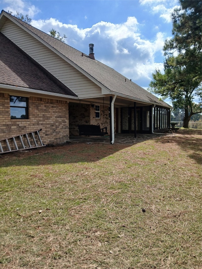 Rear view of property featuring roof with shingles, brick siding, and a lawn